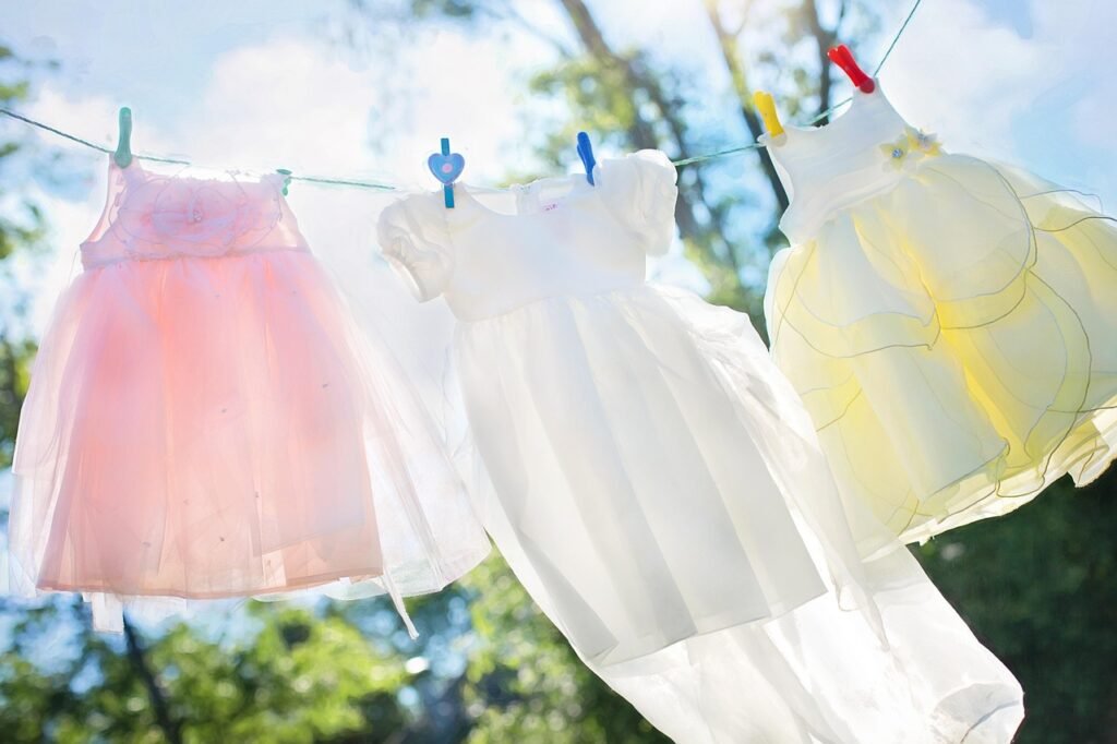 Three delicate, light-colored dresses hanging on a clothesline outdoors under a bright sun, showcasing the natural and safe air-drying results of a successful spring cleaning safety tips routine